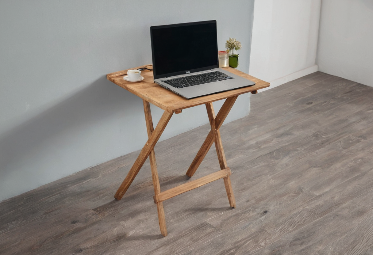 Small wooden table with crossed folding legs holding a silver laptop, white cup, and small plant near a wall.